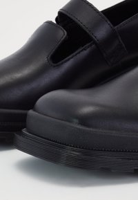 Black leather shoes with a closed toe, cutout sides, and adjustable strap; textured rubber sole with ridges for traction.