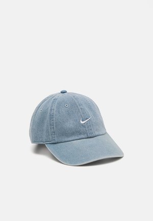 Casquette de baseball en denim bleu clair avec visière incurvée et petit logo Nike Swoosh blanc sur le panneau avant sur fond uni.