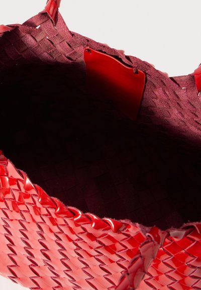 Bolsa de mão tecida em vermelho, feita de material brilhante, com forro interno texturizado e um design estruturado de abertura no topo, com etiquetas de destaque.