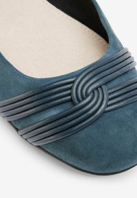 Teal mockasiner i ruggat läder med vävda detaljer och mörkblå remmar. Rund tå och slät inredning.