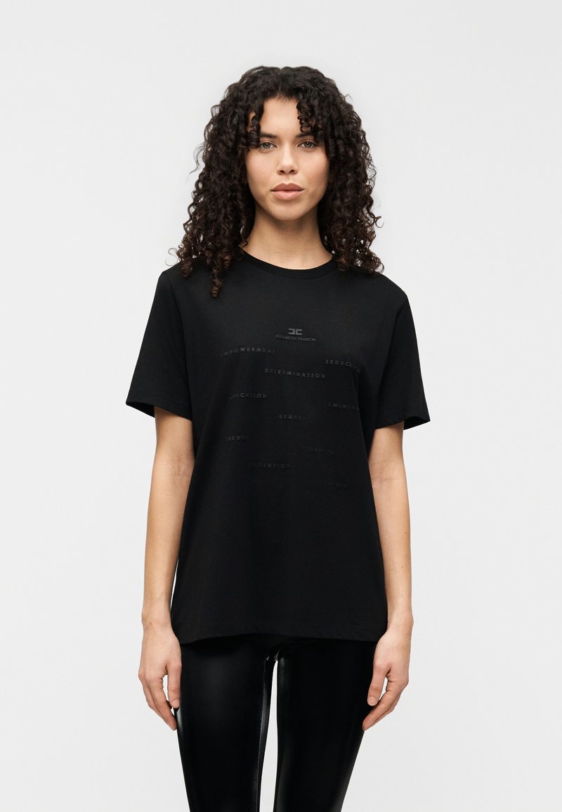 Μαύρο βαμβακερό T-shirt με στρογγυλή λαιμόκοψη, κοντά μανίκια και ανάγλυφο κείμενο σε διάφορα μεγέθη στο μπροστινό μέρος. Συνδυάζεται με γυαλιστερό μαύρο κολάν.