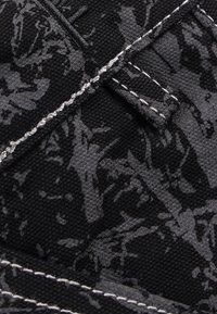 Μαύρο υλικό καμβά με γκρι αφηρημένο σχέδιο, με λευκή ραφή και μικρή υφασμάτινη ετικέτα. Η κοντινή εικόνα αποκαλύπτει τις λεπτομέρειες της υφής.