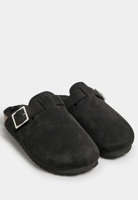 Zuecos de ante negro con punta redonda, suela plana y una correa de cuero ajustable con un detalle de hebilla en tono plateado.