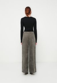 Gray wide-leg corduroy pants with a textured finish, paired with a fitted black long-sleeve top. Plain back view with no visible details.
