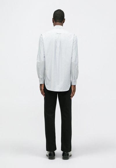 Hele sinise ja valge joonega pikkade varrukatega särk, mis sisaldab nööbiga kraed, volditud selga ja kogutud mansette. Kanda mustade pükstega.