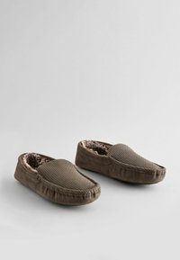 Brune ruskinds slippers med en tekstureret overdel, blød pelsforing og en rund tå. Har syningsdetaljer langs kanterne.