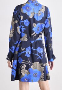 Blommig klänning med marinblå bakgrund och stora blåa och grå blommor, långa ärmar, midja med bälte och utfälld nederkant.