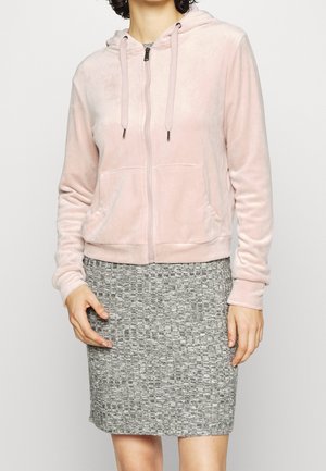 Hellrosa Zip-Hoodie aus weichem Stoff, mit Kapuze, Kordeln und seitlichen Taschen. Kombiniert mit einem strukturierten grauen Bleistiftrock.