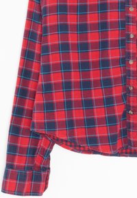 Camicia a quadri rossi e blu navy, maniche lunghe, con bottoni davanti, orlo arrotondato e strisce azzurro chiaro in contrasto intrecciate nel motivo a quadri.