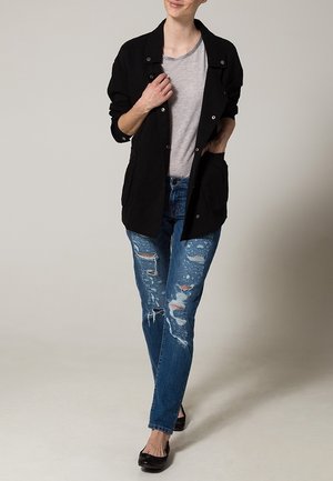 Czarna, zapinana kurtka z dwoma przednimi kieszeniami, noszona na jasnoszarym t-shircie i zniszczonych niebieskich dżinsach, uzupełniona czarnymi balerinkami.