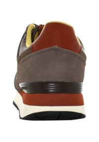 Sneaker in suede marrone con lacci gialli, pattino posteriore rosso, suola intermedia bianca e suola in gomma nera. Mostra la vista posteriore con dettagli delle cuciture.