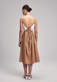 Kaksivärinen mekko, jossa on tiukka valkoinen bodice ja leikkisä beige hame. Avoin selkä, jossa on sidontatieto, valmistettu sileästä kankaasta, ja pituus polveen asti.