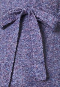 Tissu tricoté violet avec une surface texturée et un détail de nœud noué. Le matériau présente un mélange de fils plus clairs et plus foncés.