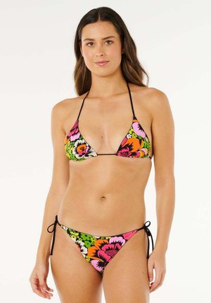 Kobieta w wielokolorowym, kwiecistym bikini typu string z czarnymi wiązaniami, stojąca na jednolitym białym tle.