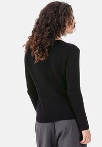 Pull noir en maille avec manches longues et silhouette ajustée. Tissu légèrement texturé, poignets et ourlet côtelés, design minimaliste.