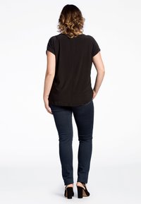 Sort kortærmet top med rund halsudskæring, bagseamsdetalje, kombineret med mørke skinny jeans og sorte hælede sandaler.