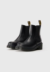Melnas ādas potītes botas ar elastīgām sānu paneļiem un dzeltenām zīmola cilpām uz papēžiem, uz baltā fona.