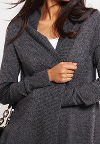 Cardigan gris tricoté avec un col en V profond, des manches longues et des poignets côtelés, présentant un devant drapé et une texture douce.