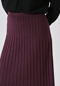 Donna che indossa una gonna a costine viola scuro abbinata a un top nero con bottoni, mostrata dalla vita in giù.