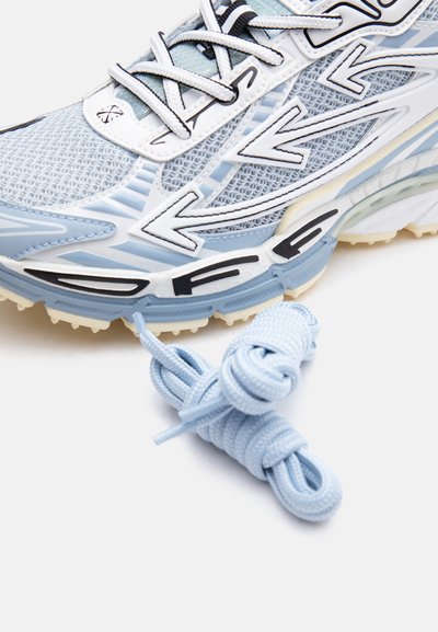 Αθλητικό παπούτσι σε ανοιχτό μπλε και λευκό με πλεκτό επάνω μέρος, επικαλύψεις σε σχήμα βέλους, μαύρο λογότυπο "DFG" στη σόλα και επιπλέον ανοιχτό μπλε κορδόνια δίπλα του.