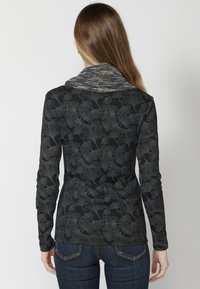 Langärmliges Oberteil in Schwarz mit einem Ginkgo-Blattmuster; hat einen strukturierten, grauen Strickkragen. Der Stoff wirkt weich und enganliegend.