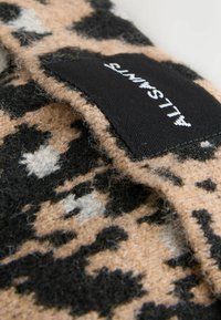 Wool blend fabric with a tan, black, and cream leopard print pattern. Features a visible black label with white text. Soft texture.