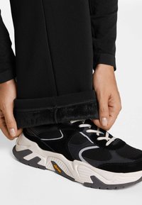 Svarta byxor med mjuka, lurviga manschetter, i kombination med svarta och vita sneakers med mesh- och mockadetaljer. Vibram-logotyp synlig på skon.