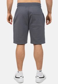 Grijze katoenen shorts met een elastische tailleband, een achterzak en een gladde textuur, gedragen met witte sneakers en enkelsokken.