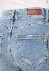 Jeans de mezclilla de corte alto en azul claro con un parche de logo LTB de cuero marrón en la parte trasera, que cuenta con dos bolsillos traseros cosidos y una textura desgastada.