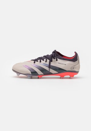 Crampon de football Adidas Predator beige avec des lacets noirs, des rayures noires et violettes, et des crampons rouges sous la semelle.