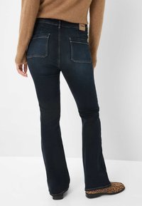 Dunkelblaue, ausgestellte Jeans mit hoher Taille, ausgestattet mit zwei Gesäßtaschen. Kombiniert mit einem braunen Strickpullover und Ankle Boots im Leopardenmuster.