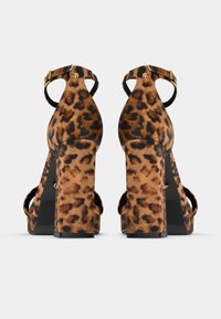 Sandalias de tacón alto con estampado de leopardo, tacón grueso, parte trasera abierta y una correa en el tobillo con hebilla dorada, confeccionadas con tela texturizada.