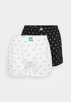 Deux paires de boxers : l'une est blanche avec un imprimé de baskets, l'autre est noire avec un design similaire. Elles disposent de tailles élastiques et de boutons à l'avant.