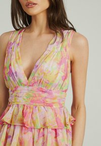 Blumengemustertes Kleid in Pastellfarben, mit tiefem V-Ausschnitt, Raffung an der Taille und Rüschensaum. Leichter Stoff.