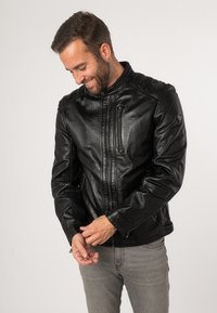 Schwarze Lederjacke mit hohem Kragen, durchgehendem Reißverschluss und Reißverschlusstaschen. Glatte Textur und taillierte Passform mit subtilen Schulternähten.