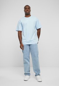 Light blue short-sleeve T-shirt with a round neck and a subtle graphic detail. Paired with light-wash jeans and white sneakers.