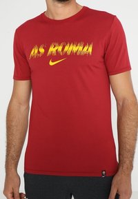 Camiseta roja de manga corta fabricada con tejido ligero. Presenta "AS ROMA" impreso en amarillo con el logo de Nike. Diseño clásico de cuello redondo.