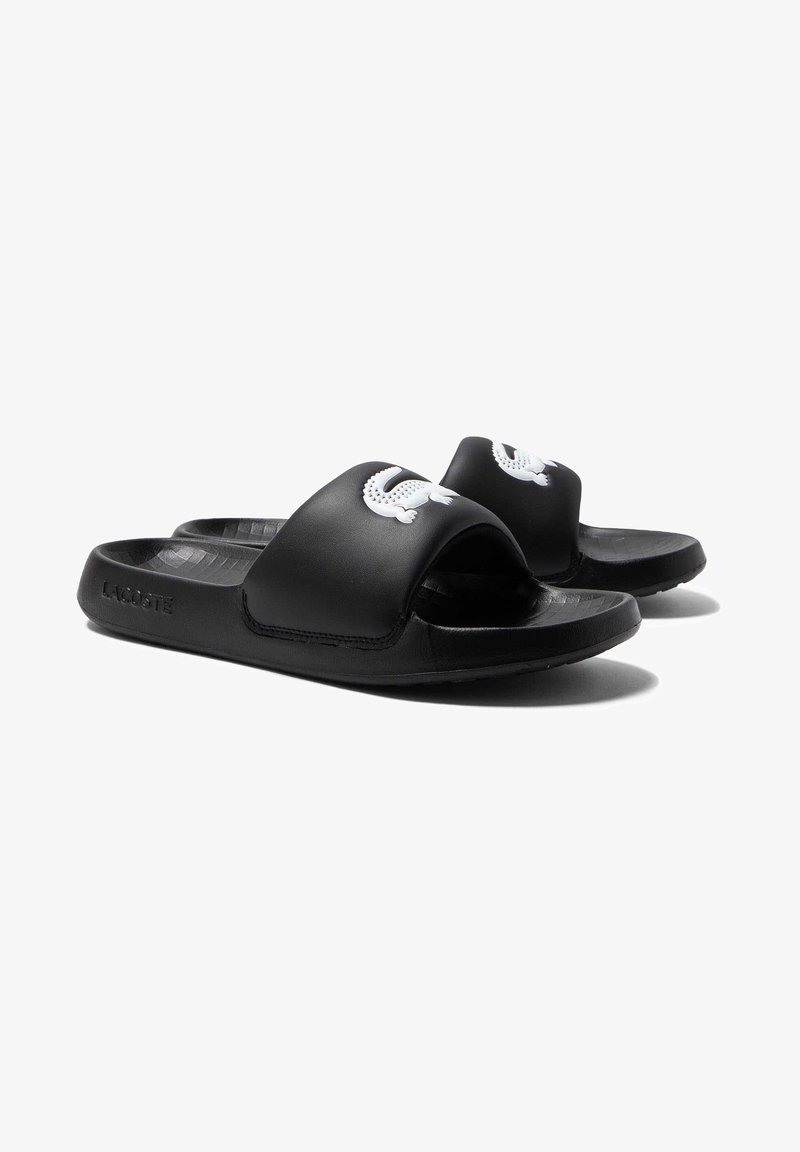 Black rubber slide sandals with a wide strap and a white logo. Textured insole and a flexible sole for comfort.