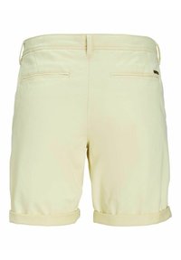 Světlé žluté šortky s ohrnutými manžetami, obsahující dvě zadní kapsy a decentní logo detail na pásku. Hladká textilie.
