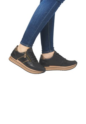 Schwarze Leder-Sneaker mit einem braunen Akzent, ausgestattet mit einem seitlichen Reißverschluss, strukturierten Einsätzen und einer gerippten Sohle. Getragen mit blauen Jeans.