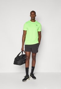 Neon green short-sleeve shirt, black shorts, black sports socks, and black sneakers with green accents. Carrying a black duffle bag.