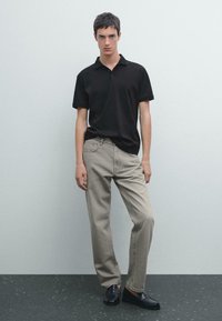 Sort polo-shirt, beige brede bukser og sorte loafers. Glat stof, klassisk krave og diskret syning på bukserne.