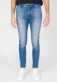 Jeans de mezclilla azul claro con un ajuste slim, que presentan un desvanecimiento sutil, cinco bolsillos y un cierre de botones, combinados con zapatillas blancas.