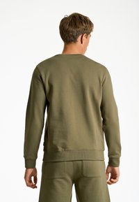 Sudadera verde oliva con mangas largas, puños y dobladillo acanalados, hecha de una mezcla de algodón texturizado. Diseñada con un sencillo cuello redondo.