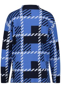 Niebieski i czarny, oversize'owy sweter z geometrycznym wzorem w kratę, z ukośnymi i prostymi białymi paskami.