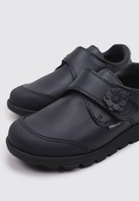 Zapatos de cuero negros con puntera redonda, correa ajustable lateral y un acento de flor en el empeine; detalles texturizados en la punta.