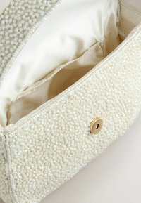Petit sac pochette blanc à perles avec un bouton pression magnétique doré et une doublure en tissu beige à l'intérieur.