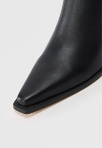 Botín de cuero negro con punta afilada, textura suave, diseño minimalista y tacón bajo y rectangular.