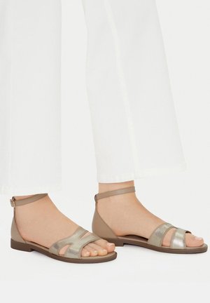 Páskové sandály kombinující světle hnědé a kovově stříbrné materiály, s plochou podrážkou, otevřenou špičkou, páskem kolem kotníku a výřezy.