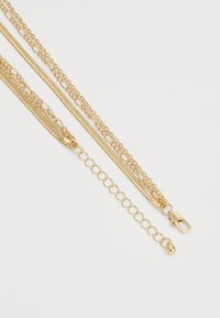 Collier en chaîne dorée plaqué or, mettant en avant des maillons fins, des styles de chaînes mélangés et un fermoir mousqueton agrémenté d'un petit détail en perle.